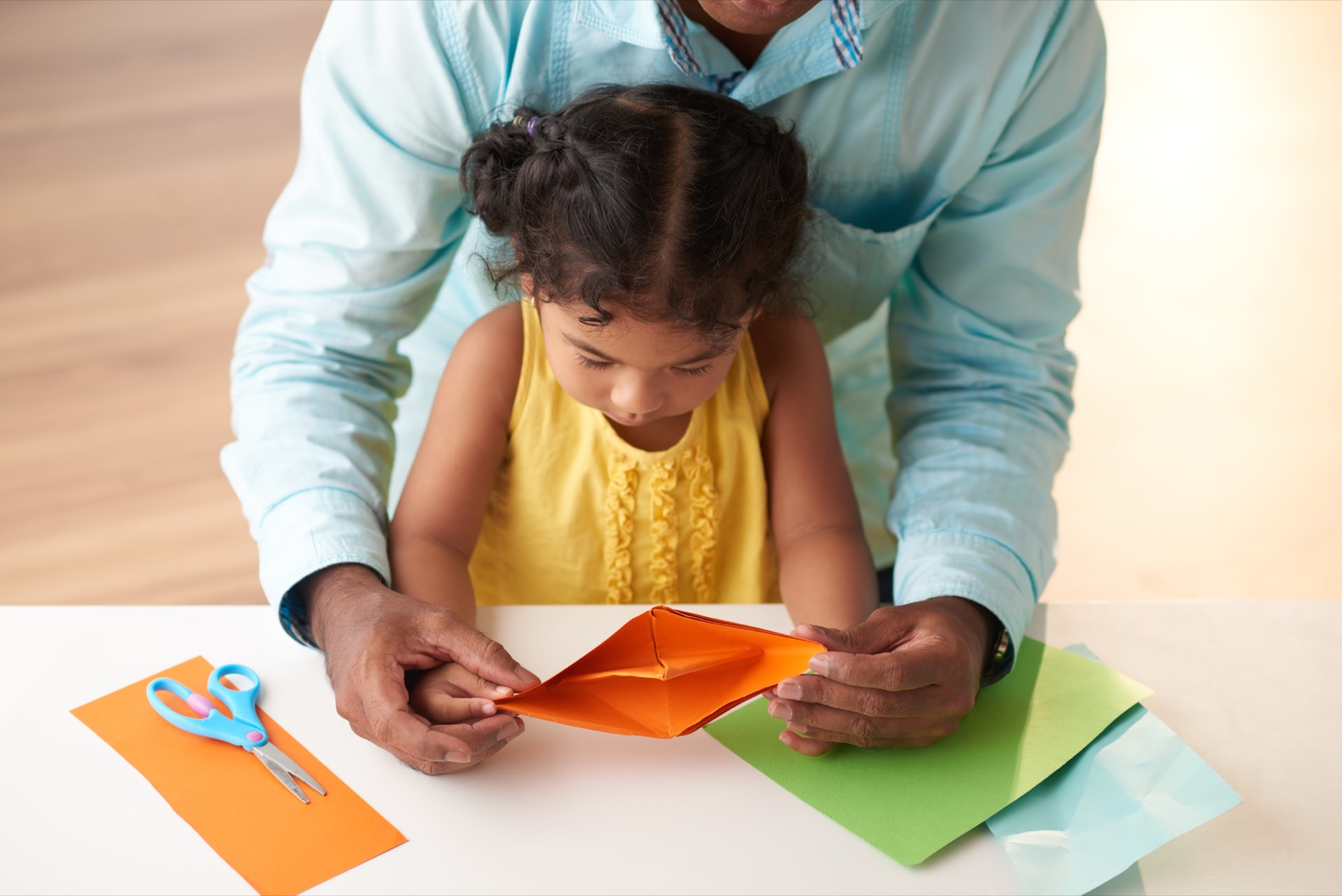 A father and daughter folding colourful paper together