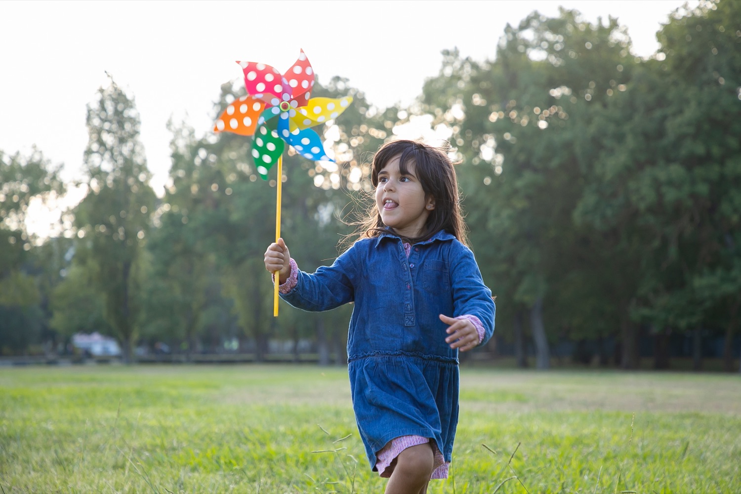 A girl runs across the grass holding a rainbow pinwheel